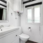 Badezimmer mit Waschbecken, Toilette und Dusche. Fenster und Spiegel sichtbar.
