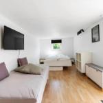 Zimmer mit zwei Betten, Wand-TV und Holzboden. Fenster mit Blick auf Grün.