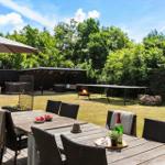 Hinterhof mit Grill, Tisch, Stühlen und Sonnenschirm. Grasfläche und Bäume im Hintergrund.