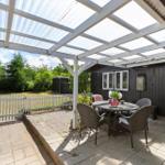 Terrasse mit Tisch und Stühlen unter weißem Dach. Hinterhof mit weißen Zaun und Bäumen.