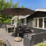 Terrasse mit Sitzgruppe, Tisch, Sonnenschutz und Grill. Schwarze Holzfassade und Fenster.