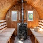 Sauna mit Holzbank, Holzwand und Ofen mit Steinen.