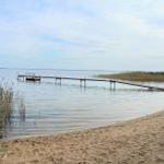Ein hölzerner Steg führt vom Strand in einen ruhigen See.