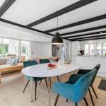Essbereich mit blauen Stühlen und weißem Tisch. Wohnbereich mit Sofa und Holztisch. Küche mit Arbeitsplatte.