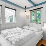 Schlafzimmer mit weißem Bett, Holzboden und Fenstern mit Blick auf Grün.
