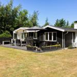 Haus mit Terrasse, Garten und Grillplatz unter blauem Himmel.