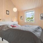 Schlafzimmer mit Holzwand, weißem Bett und Fenster mit Blick auf Außenbereich.