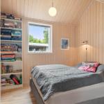 Schlafzimmer mit Holzwand, Bett, Fenster und Bücherregal.