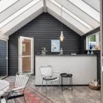 Terrasse mit Sitzgelegenheiten, Bar und Glasdach. Schwarze Holzwände und weiße Möbel.