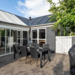 Terrasse mit Tisch und Stühlen, Glasveranda und Grillplatz. Hinterhof mit weißem Tor und Baum.