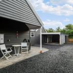 Haus mit Terrasse, weißem Tisch und Stühlen, Carport und Kiesfläche.