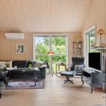 Wohnzimmer mit Sofa, Sessel und Fernseher. Holzwände und große Fenster.