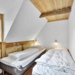 Zwei Betten in einem Dachzimmer mit Holzdecke und Fenster.