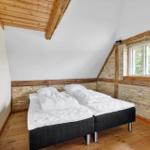 Zimmer mit Doppelbett, Holzdecke und Fenster. Wandgestaltung mit Stein und Holz.