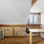 Schlafzimmer mit Holztisch, Stuhl und Fenster. Wand aus Ziegel und Holz.