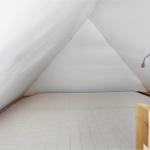 Schlafzimmer mit Dachschrägen, Holzbett und lila Wandlampe.