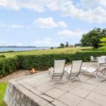 Terrasse mit Sitzgelegenheiten und Grillplatz. Blick auf Felder und Wasser.