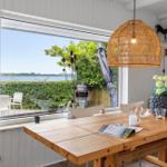Holztisch mit Stühlen und Blick auf den Garten. Wicker-Lampe und Blumenarrangement.