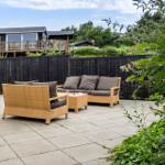 Terrasse mit Sitzgruppe, schwarzer Zaun und Gartenhaus im Hintergrund.