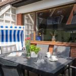Terrasse mit Tisch, Stühlen und blau-weißem Sonnenschirm. Fenster reflektiert Nachbarhäuser.