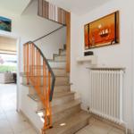 Treppe mit orangefarbener Balustrade führt nach oben. An den Wänden hängen Bilder.