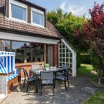 Terrasse mit Tisch, Stühlen und Strandkorb. Hinterhof mit Bäumen und rotem Laub.