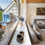 Wohnbereich mit Sofa und Fensterblick auf Terrasse mit Strandkorb.