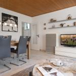 Essbereich mit Tisch und Stühlen, Wohnbereich mit Fernseher und Regalen.