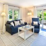 Living room with sofa, armchair, and table. Entrance to terrace with garden view.