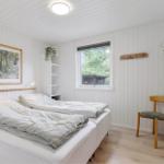 Schlafzimmer mit Bett, Stuhl, Spiegel und Fenster mit Blick auf Wald.