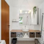 Badezimmer mit Waschtisch, Spiegel und Dusche. Holzunterschrank und Pflanze.