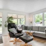 Wohnzimmer mit grauem Sofa, schwarzer Ledersessel und großem Fensterblick auf Garten.