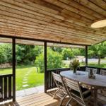 Terrasse mit Holzdecke, Tisch und Stühlen. Blick auf grünen Garten mit Weg.