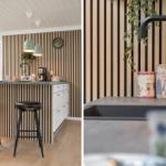 Küche mit Holzwand, Barhocker und Arbeitsplatte. Wasserhahn und Behälter sind sichtbar.