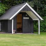 Schwarze Sauna mit Schild BEDSTES HYTE in grünem Garten