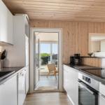 Küche mit weißen Schränken, dunklem Arbeitsplatz und Holzwand. Durchgang zur Terrasse mit Stuhl.