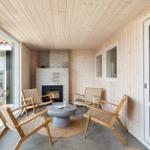 Terrasse mit Holzwänden, Kamin und vier Sitzgelegenheiten. Durchgehende Glasfronten.