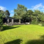 Moderne Villa mit Terrasse, Garten und Bäumen unter blauem Himmel.
