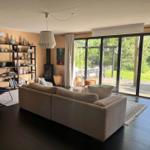 Wohnzimmer mit Sofa, Bücherregal und Glasfront zum Garten.