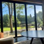 Große Glasfront mit Blick auf einen Garten mit Tisch und Stühlen.