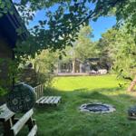 Grüner Garten mit Feuerkorb, Holzbank und Pavillon im Hintergrund.