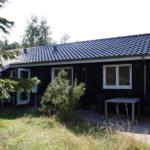 Schwarzes Holzhaus mit Terrasse, Tisch und Stühlen. Umgeben von Bäumen und Gras.