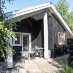 Schwarzes Holzhaus mit Terrasse, Grill und Garten. Fenster und Tür sind weiß.