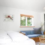 Schlafzimmer mit Bett, Sofa und Fenster mit Blick auf Wald.