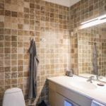 Badezimmer mit braunen Fliesen, Waschtisch und Spiegel.