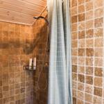 Dusche mit braunen Fliesen, Holzdecke und grauem Duschvorhang.