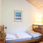 Ein Schlafzimmer mit Holzbett, Wandbild und Fenster mit Pflanze.