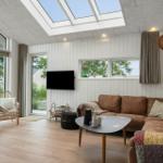 Wohnzimmer mit braunem Sofa, runden Tisch und großen Fenstern. Deckenfenster und Holzboden.