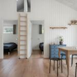 Wohnraum mit Treppe, Schlafzimmer und Esstisch. Holzdielen und weiße Wände.