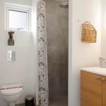Badezimmer mit Dusche, Waschbecken und Toilette. Wandspiegel und Korb sind sichtbar.